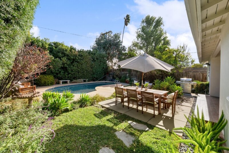 Uređeno dvorište sa bazenom, drvenim stolom i stolicama, velikim suncobranom i zelenilom oko prostora za sedenje