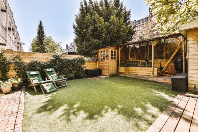 Uređeno malo dvorište sa veštačkom travom, drvenom pergolom, baštenskom kućicom i ležaljkama za odmor