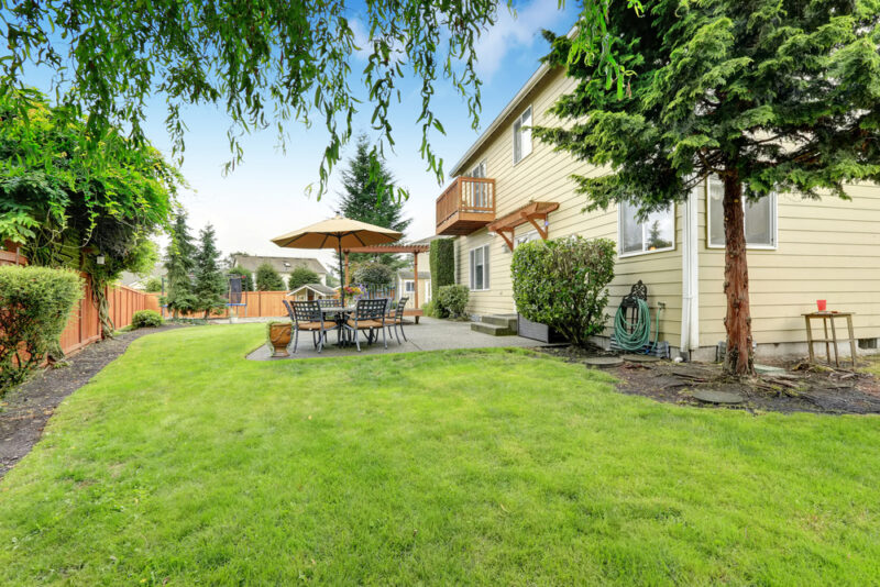 Prostrano dvorište porodične kuće sa zelenim travnjakom, baštenskim nameštajem i velikim suncobranom pored terase